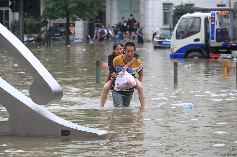 Man carrying a woman wades through a flooded road following heavy rainfall in Zhengzhou  / CHINA DAILY