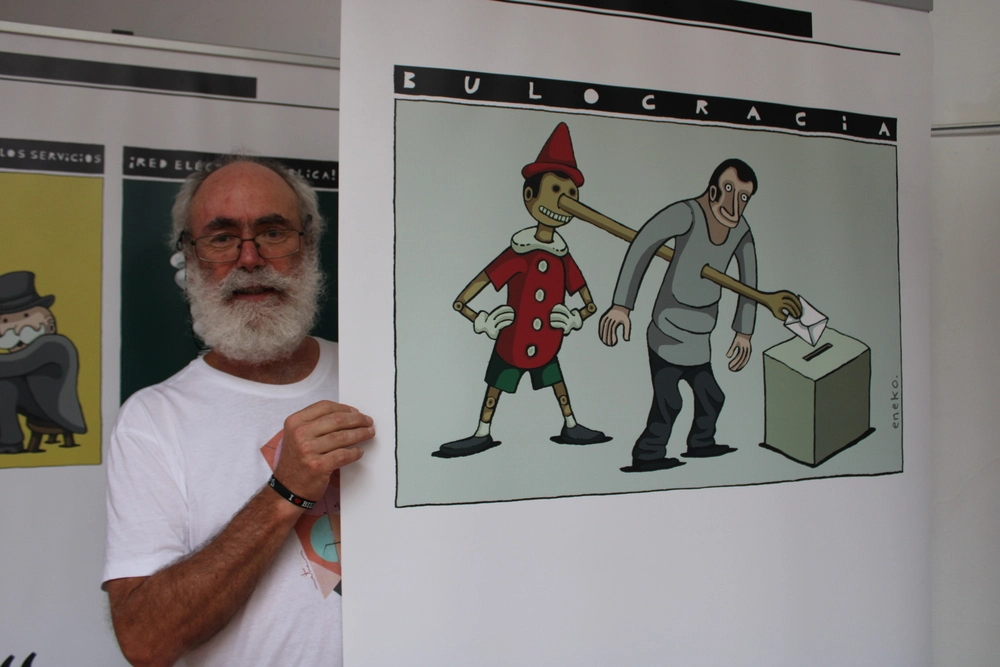 El artista de humor gráfico ENEKO junto a una impresión de sus dibujos editoriales, Foto: RIÁNSARES L.C. publicada en latribunadecuenca.es